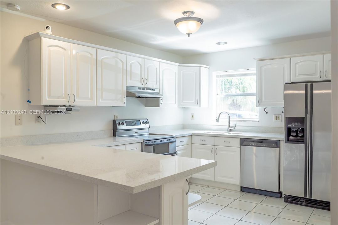 Kitchen featuring white cabinetry, solid-surface countertops with a breakfast bar, stainless steel appliances, and tile flooring