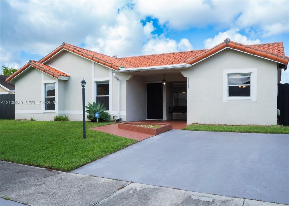 Stucco exterior residence featuring a terracotta-tiled roof, covered entryway, and concrete driveway