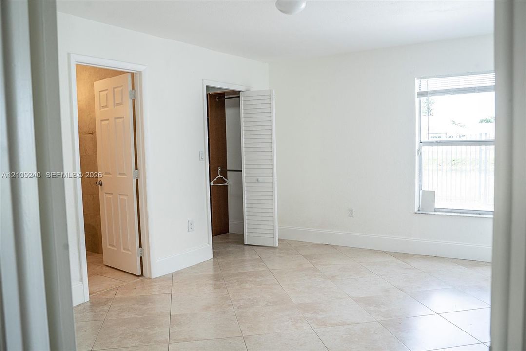 Neutral-toned ceramic tile flooring, interior closet with louvered doors, and a single-hung window with white frame