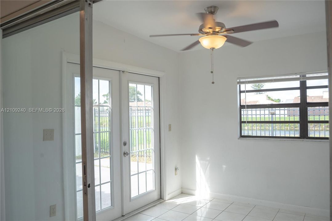 Room featuring white ceramic tile flooring, French doors with glass panes, a ceiling fan with integrated lighting, and a multi-pane window