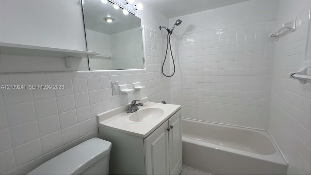 Bathroom featuring a white vanity cabinet with an integrated basin, a wall-mounted medicine cabinet with integrated lighting, and a full-height tiled shower surround