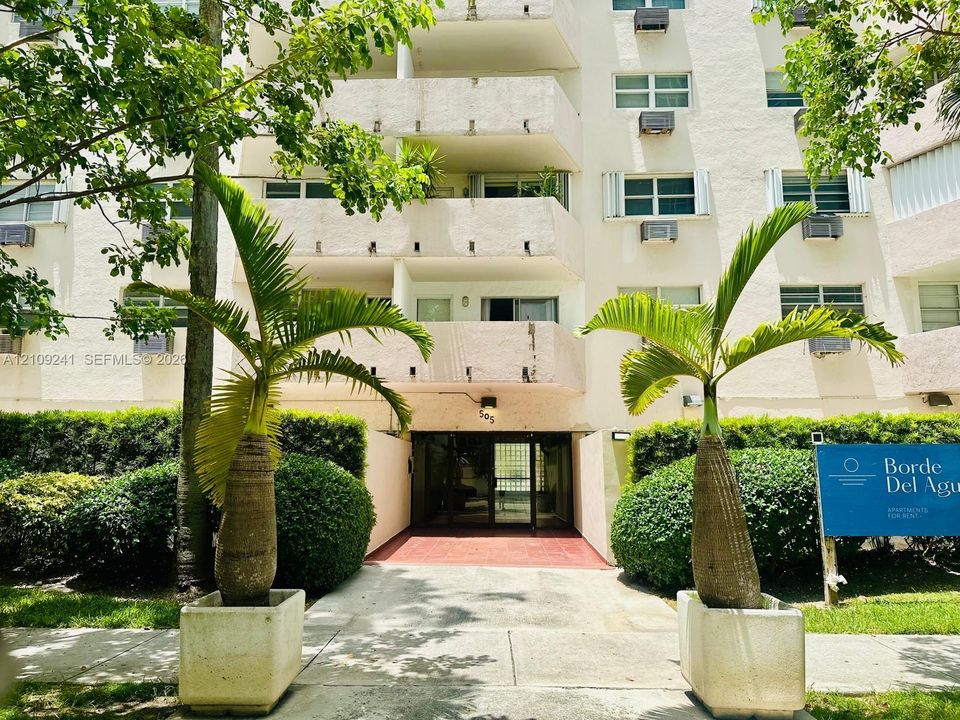 Multi-story residential building exterior featuring a stucco façade, private recessed balconies, and a covered entry with tiled flooring