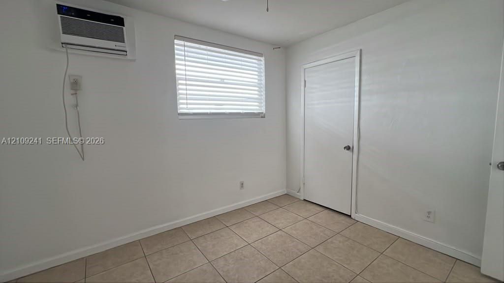 Interior room featuring neutral ceramic tile flooring, a window with horizontal blinds, and a wall-mounted air conditioning unit