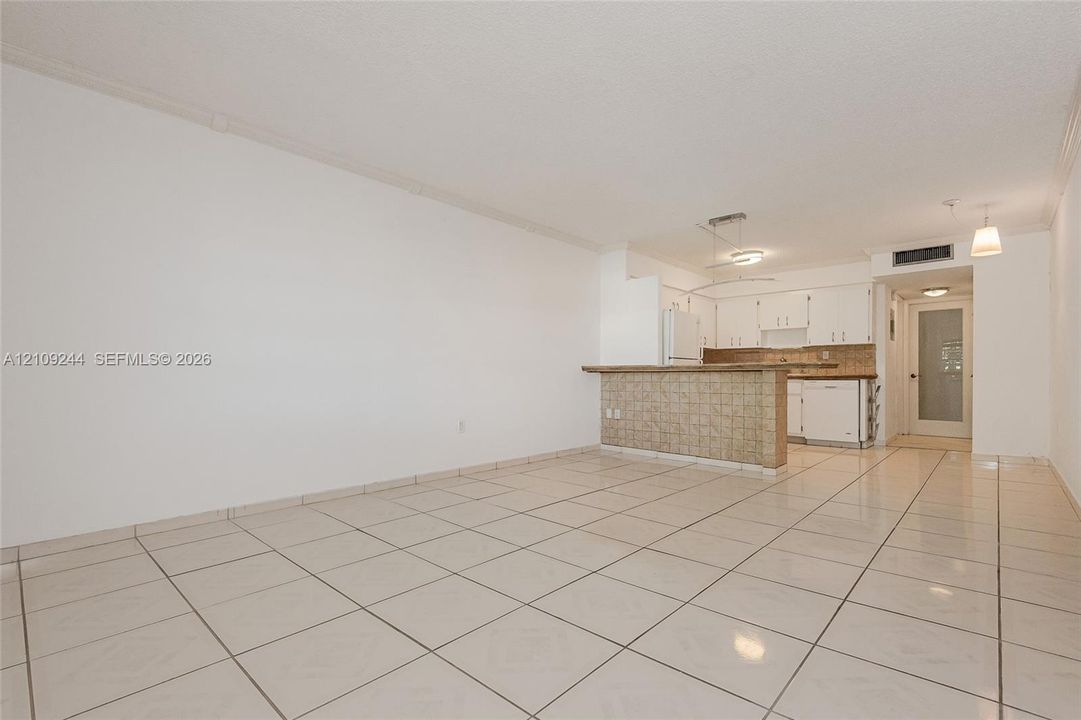 Open-concept interior featuring light-colored tile flooring, breakfast bar with tile detailing, white cabinetry, and pendant lighting