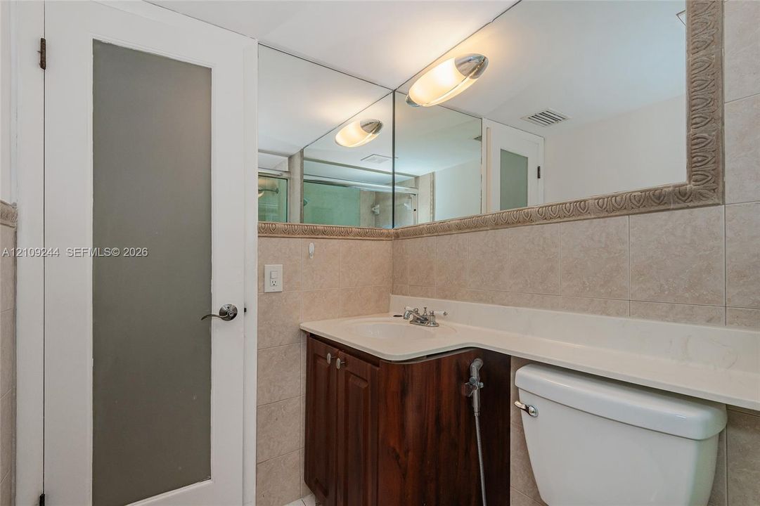 Bathroom featuring a dark wood-finish vanity with a surface-mounted sink, wall-to-wall mirror, tiled walls, and a door with a frosted glass panel