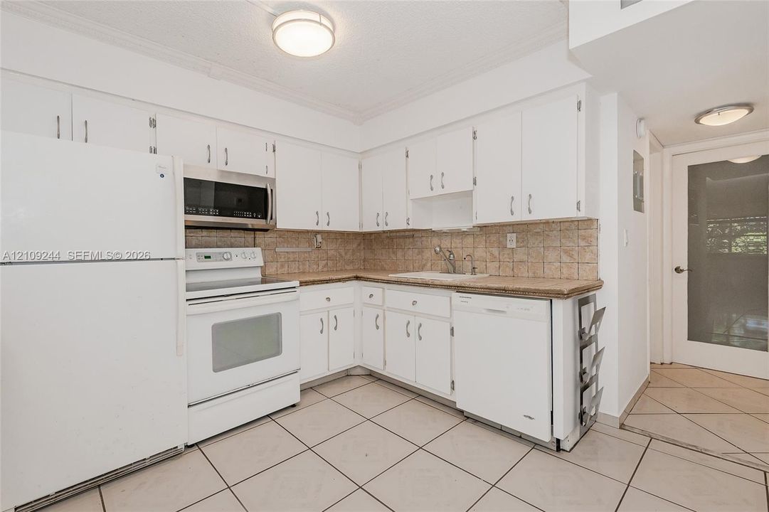 Kitchen featuring white cabinetry, solid-surface countertops, tile backsplash, tile flooring, and integrated white appliances