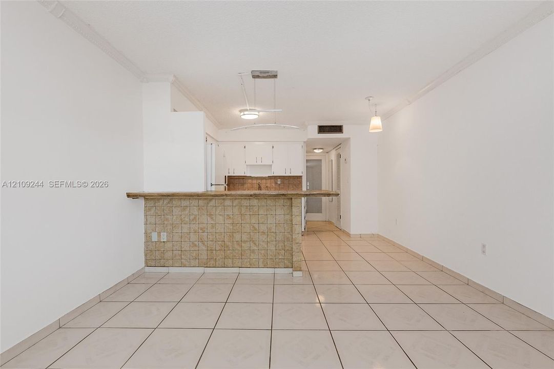 Open floor plan featuring ceramic tile flooring, a breakfast bar with decorative tile cladding, white upper cabinetry, and suspended pendant lighting
