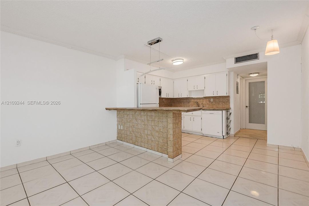 Kitchen featuring a tiled breakfast bar, white cabinetry, integrated appliances, and neutral tile flooring
