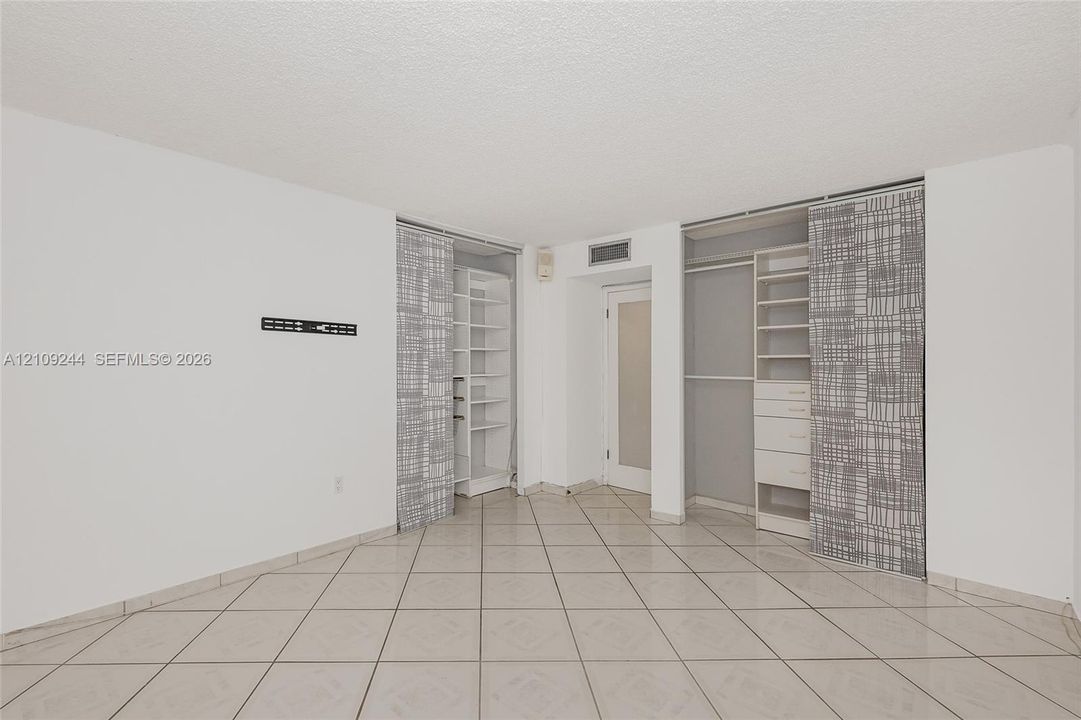 Tile flooring, dual reach-in closets featuring built-in shelving and drawer storage, and a single-panel interior door with a frosted glass insert