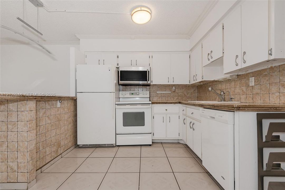 Kitchen featuring white cabinetry, tile backsplash, tile flooring, and integrated white appliances including a dishwasher, range, and microwave