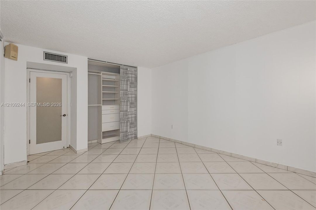 Ceramic tile flooring arranged in a diagonal pattern, interior door with a frosted glass panel, and custom built-in closet organization system featuring shelving and integrated drawers
