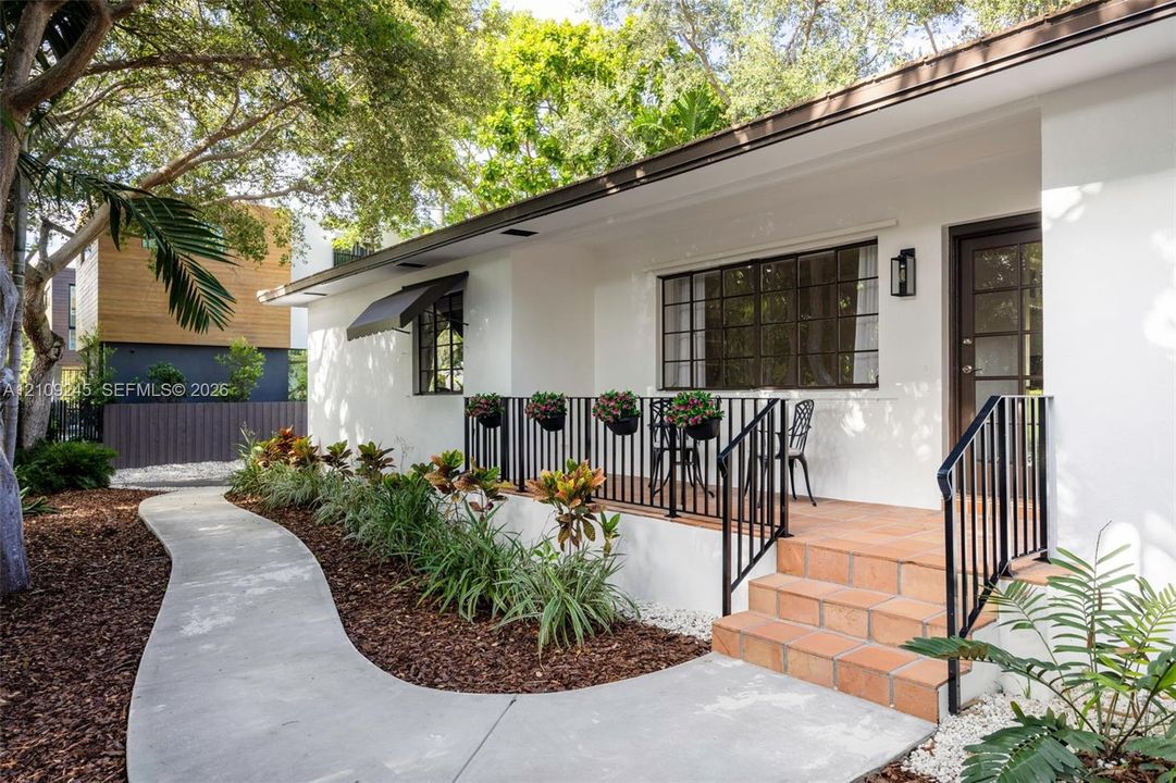 Exterior featuring white stucco siding, a terracotta-tiled front porch, black metal railings, and a curved concrete walkway