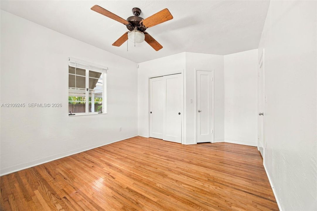 Interior room featuring wood-finish flooring, a multi-blade ceiling fan with central lighting, dual sliding closet doors, and a single-panel interior door