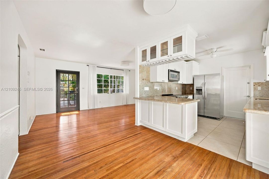 Kitchen featuring white shaker-style cabinetry, stone countertops, stainless steel appliances, wood-finish flooring, and a glass-paneled exterior door