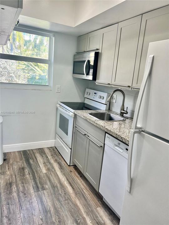 Kitchen featuring shaker-style cabinetry, stone-finish countertops, stainless steel undermount sink with gooseneck faucet, built-in stainless steel microwave, and wood-finish flooring