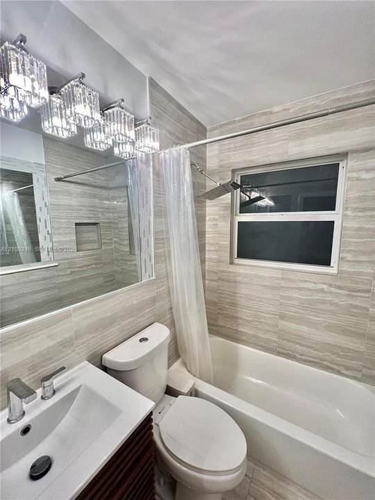 Full-wall neutral stone-look tiling, multi-light glass vanity fixture, integrated shower niche, rectangular vessel sink with chrome faucet, and overhead rainfall shower head
