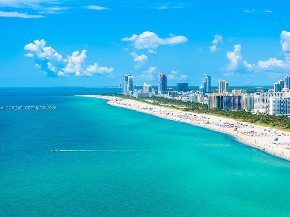 Aerial perspective of an expansive sandy coastline featuring turquoise ocean waters and an extensive metropolitan skyline