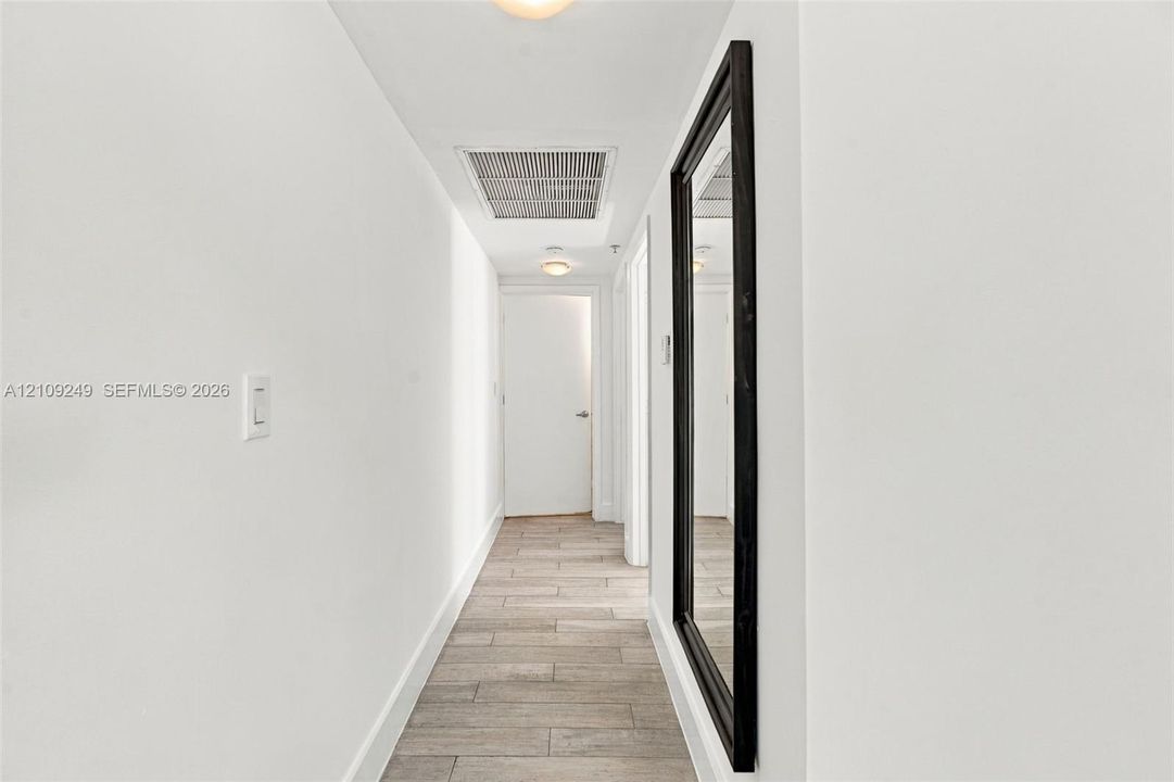 Hallway featuring wood-finish tile flooring, a recessed ceiling light, and a wall-mounted full-length mirror with a dark frame