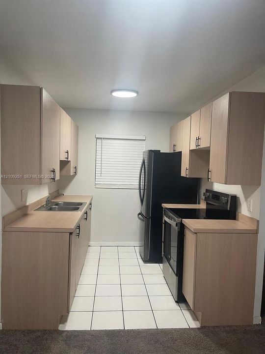 Kitchen featuring light-finish cabinetry, black appliances, solid-surface countertops, dual-basin stainless steel sink, and ceramic tile flooring