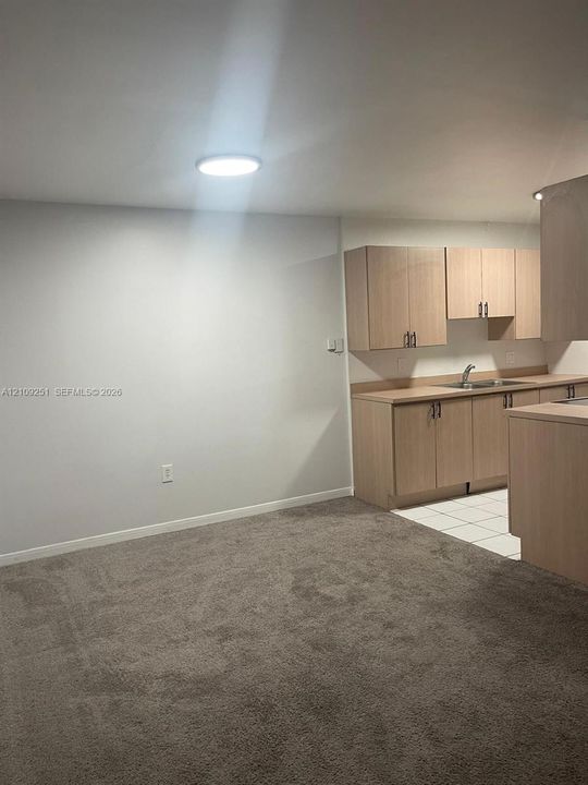 Kitchen featuring light wood-finish cabinetry, neutral countertop, stainless steel sink, and ceramic tile flooring, complemented by wall-to-wall carpeting and flush-mount overhead lighting