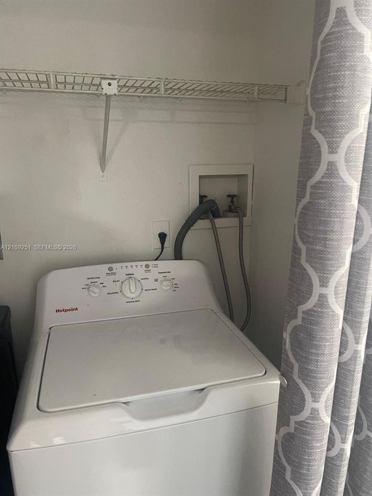 Laundry alcove featuring white top-loading washing machine, recessed water hookups, and wire shelving