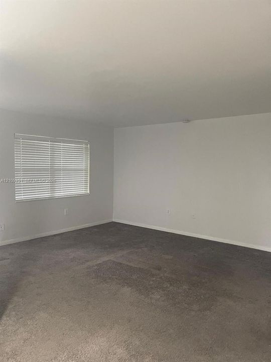 Neutral-toned carpet flooring, smooth walls, and a window fitted with horizontal blinds
