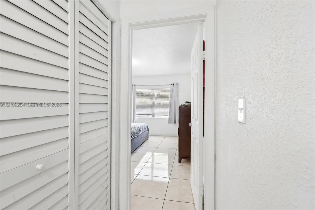 White louvered bi-fold closet doors and neutral large-format tile flooring