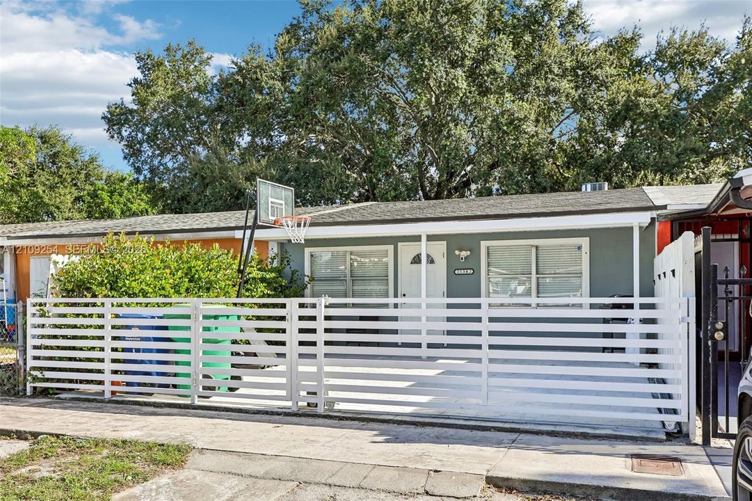 Single-story exterior featuring a horizontal slat privacy fence, concrete paved front area, and mature canopy trees