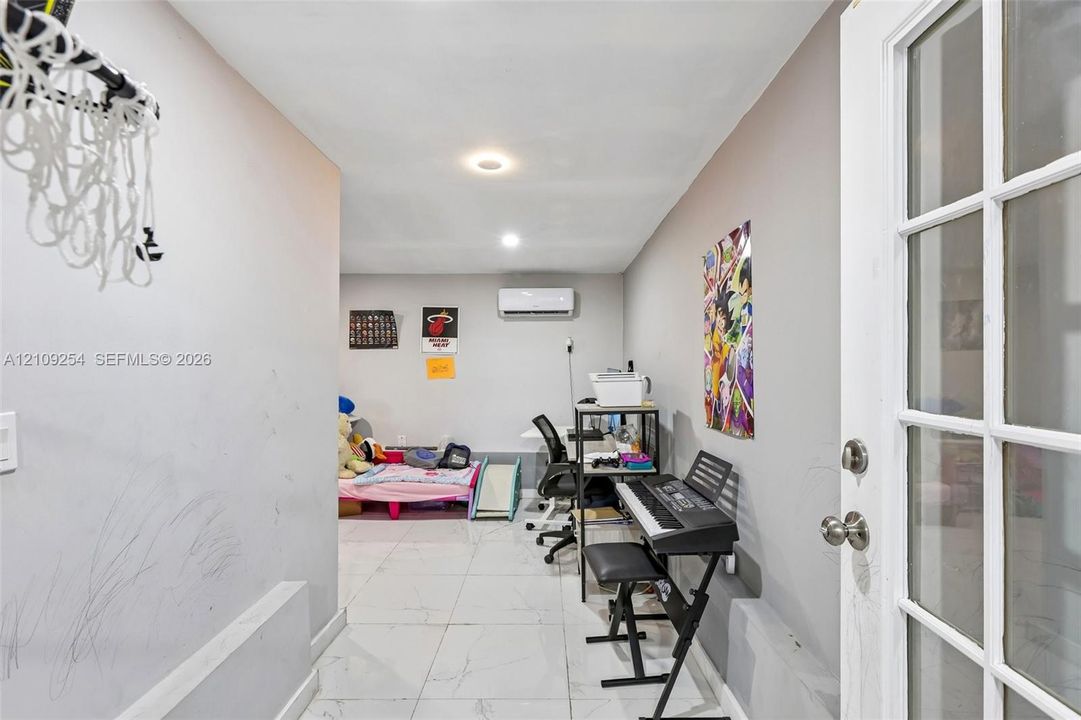 Interior room featuring large-format light-toned tile flooring, recessed lighting, and a wall-mounted ductless air conditioning unit, accessible via a glass-paneled entry door