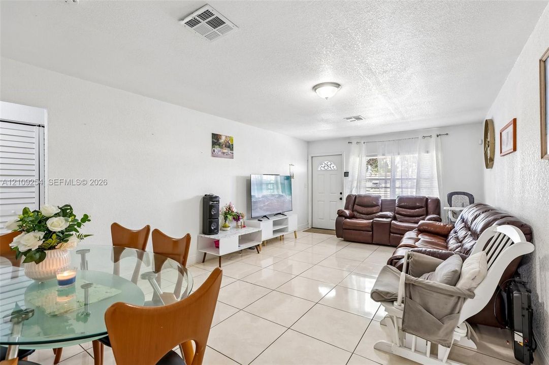 Open floor plan featuring large-format ceramic tile flooring, neutral wall finishes, a flush-mount ceiling light fixture, and a window with white casing