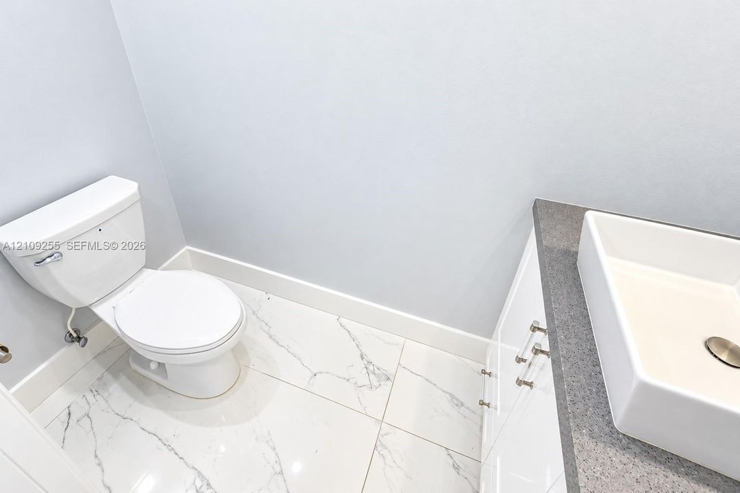 Bathroom featuring large-format tile flooring with marble-finish veining, white cabinetry, a neutral stone-finish countertop, and a rectangular vessel sink