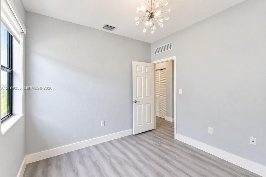 Neutral-toned room featuring wood-finish flooring, a multi-light starburst chandelier, a six-panel door, and a black-framed window