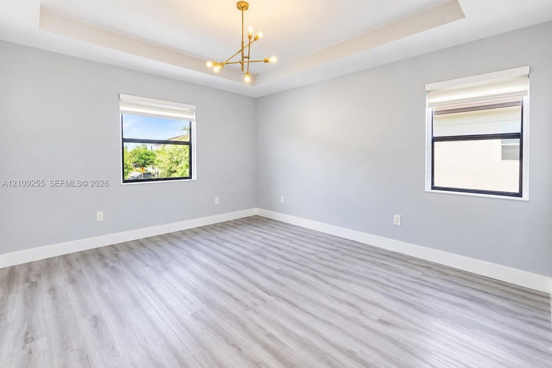 Room featuring a tray ceiling, wood-finish flooring, gold-tone multi-arm chandelier, and large windows with integrated roller shades