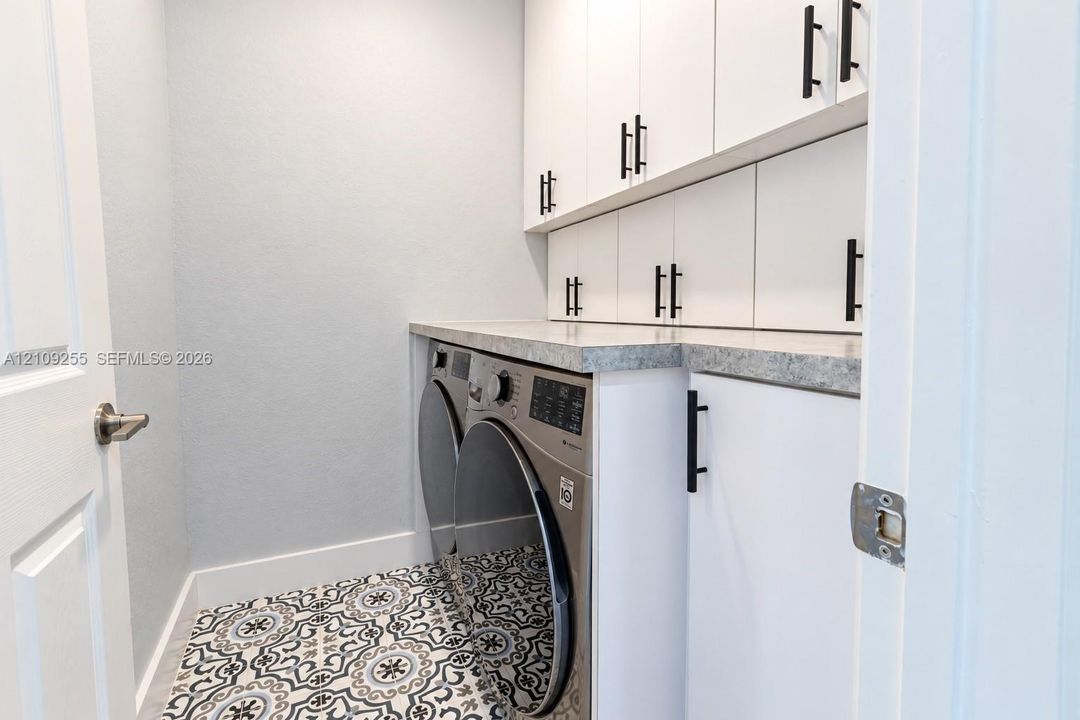 Utility space featuring white shaker-style cabinetry, matte black hardware, stone-finish countertops, and patterned tile flooring