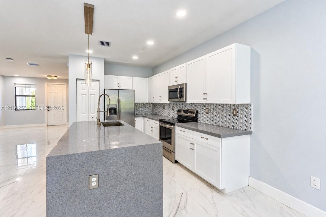 Kitchen featuring white cabinetry, solid-surface countertops, stainless steel appliances, a mosaic tile backsplash, and polished tile flooring