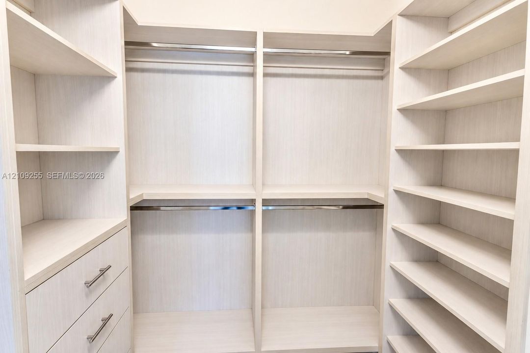 Custom walk-in closet featuring light-toned cabinetry, built-in shelving units, integrated hanging rods, and stacked storage drawers with metallic hardware