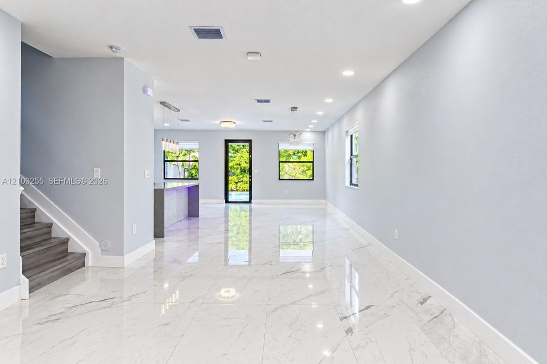 Open-concept interior featuring large-format polished tile flooring, recessed ceiling lighting, a kitchen island with integrated lighting, and a staircase with wood-finish treads