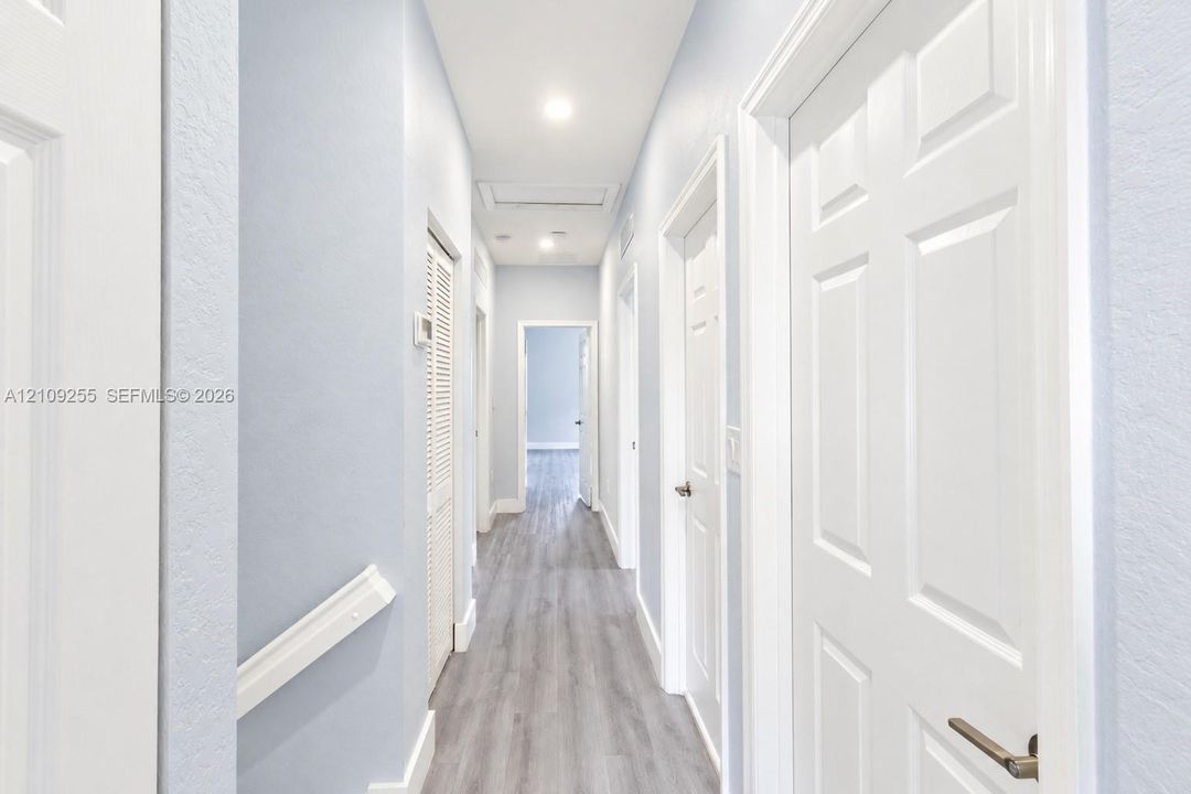 Hallway featuring wood-finish flooring, white panel doors, recessed ceiling lighting, and louvered closet cabinetry