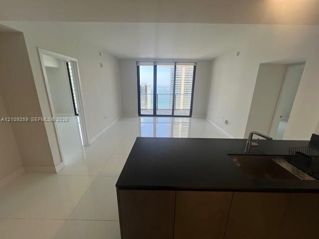 Open-concept living space featuring high-gloss tile flooring, floor-to-ceiling windows, and kitchen island with stone-finish countertop and integrated stainless steel sink