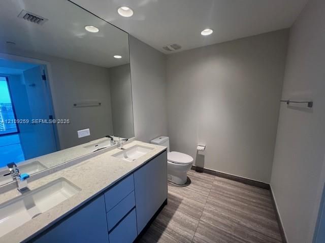 Double vanity featuring dual rectangular under-mount sinks, light-toned stone-finish countertops, flat-panel cabinetry, and large-format tile flooring
