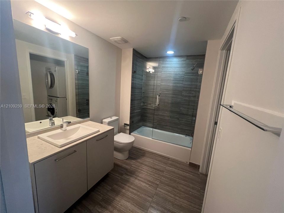 Bathroom featuring a floating vanity with a rectangular sink, quartz countertop, large wall-mounted mirror, and tub-shower combination with floor-to-ceiling tile surround