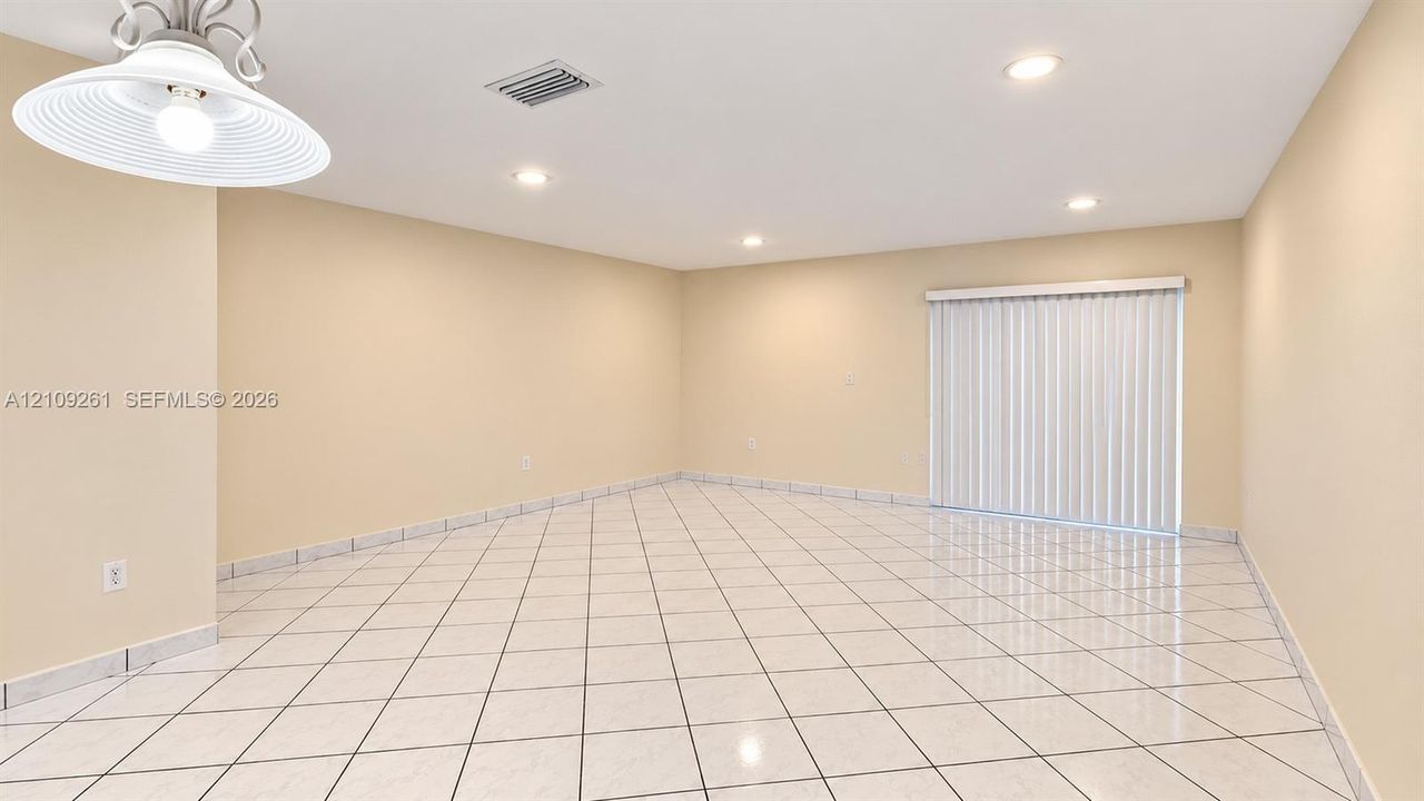 Interior space featuring neutral-toned walls, tile flooring, recessed lighting, a decorative hanging pendant light, and sliding glass doors with vertical blinds