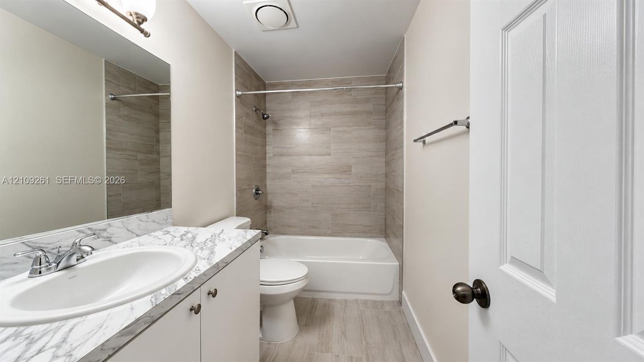 Full bathroom featuring a vanity with a stone-patterned countertop, an integrated sink, a bathtub with a tiled surround, and wood-finish tile flooring