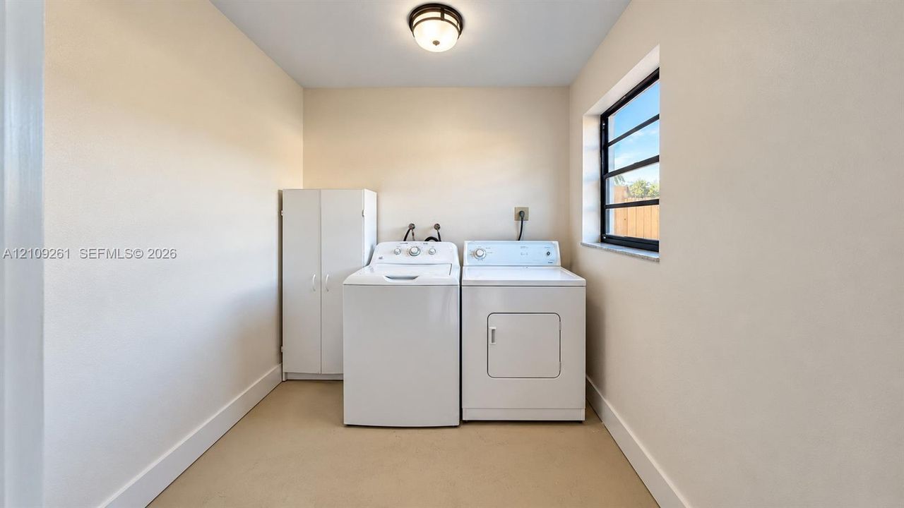 Laundry area featuring a built-in white storage cabinet, a window with multi-pane glazing, and a flush-mount ceiling light fixture