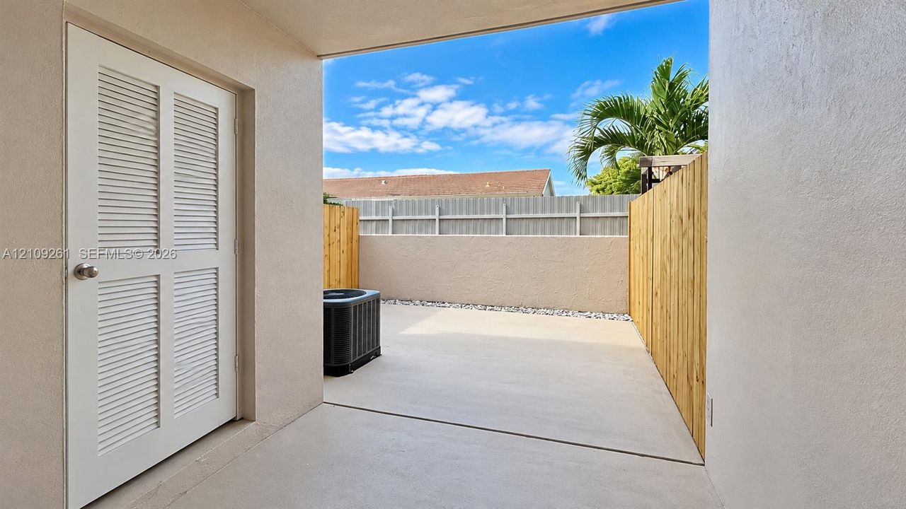 Concrete patio with wood-slat privacy fencing, exterior louvered access door, and decorative rock border
