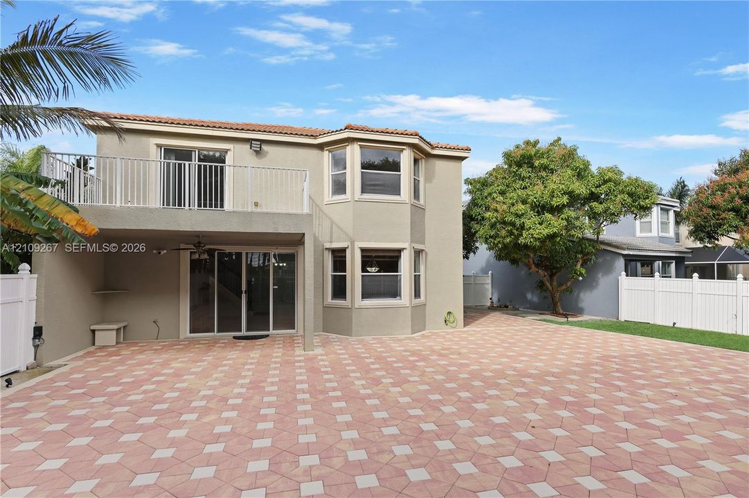Two-story exterior featuring a stucco facade, expansive paver patio, second-level balcony with white railings, and multi-pane bay windows
