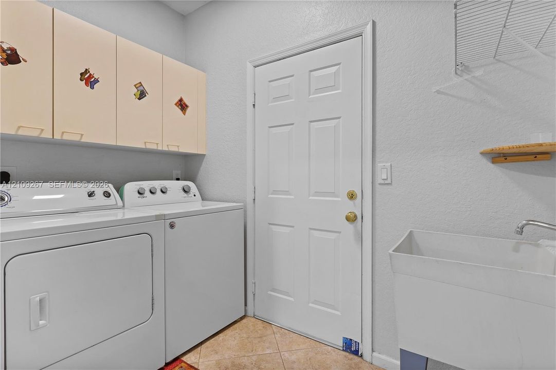 Utility area featuring wall-mounted upper cabinetry, a thermoplastic utility sink with a chrome faucet, tile flooring, and integrated overhead wire shelving