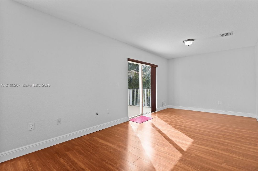 Interior space featuring wood-finish flooring, neutral wall tones, a ceiling-mounted light fixture, and sliding glass doors with access to an exterior balcony