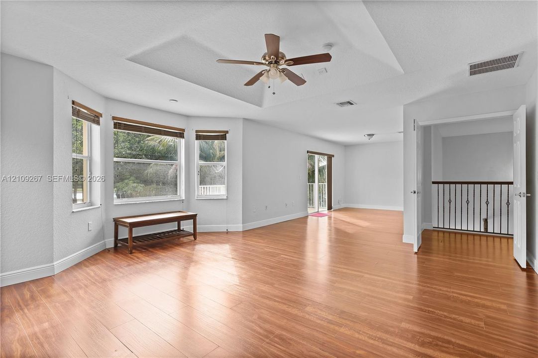 Room featuring wood-finish flooring, a tray ceiling with a multi-blade ceiling fan, and a bay window configuration