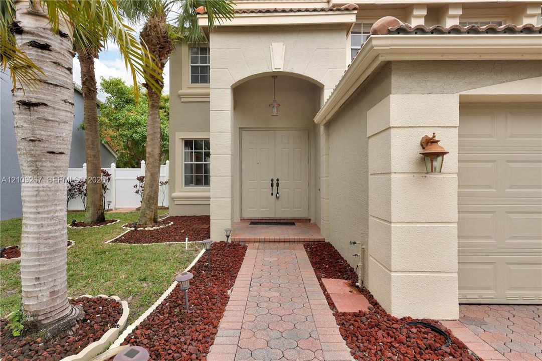 Stucco exterior featuring an arched entryway, double front doors, a paved walkway, and a multi-car garage